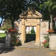 Kirchplatz in Siddessen Historischer Torbogen aus Sandstein mit Blumen, flankiert von Bäumen, führt zu einem gepflegten Platz.