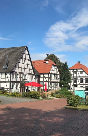 Fachwerkhäuser in Gehrden mit roten Sonnenschirmen, umgeben von Bäumen unter einem blauen Himmel.