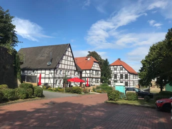 Gehrden Fachwerkhäuser in Gehrden mit roten Sonnenschirmen, umgeben von Bäumen unter einem blauen Himmel.