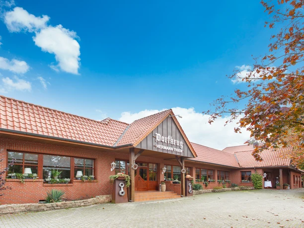 Backsteinbau mit rotem Ziegeldach, Eingang des Gasthauses Dorfkrug Thien unter blauem Himmel.