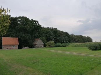 Hof Bockhop Ein alter Bauernhof mit Feldsteinhaus und rotem Dach eingebettet in eine grüne, bewaldete Landschaft.
