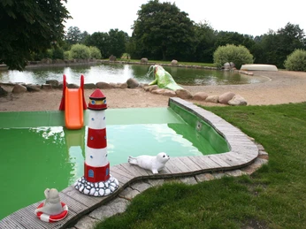 Naturfreibad Pennigsehl mit rutschender Kinderrutsche, Leuchtturm-Skulpturen und grünem Rasen.