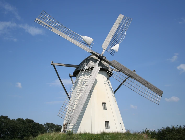 Windmühle Großenheerse Eine weiße Holländerwindmühle mit Holzflügeln erhebt sich majestätisch vor einem klaren blauen Himmel.