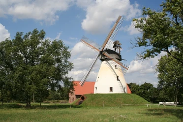 Windmühle Heimsen Windmühle Heimsen mit rotem Dach und großen Flügeln umgeben von Bäumen unter blauem Himmel.