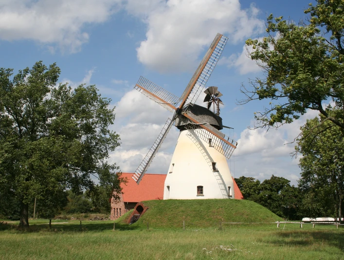 Windmühle Heimsen Windmühle Heimsen mit rotem Dach und großen Flügeln umgeben von Bäumen unter blauem Himmel.