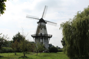 Windmühle in Lavelsloh mit markantem Flügelrad, umgeben von Bäumen und grüner Landschaft.