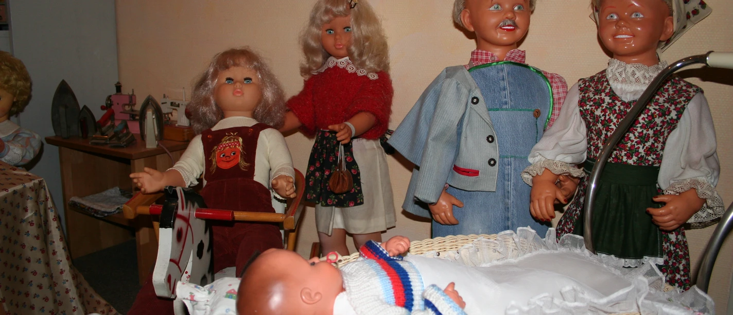 Eine Gruppe fröhlicher Puppen in traditioneller Kleidung umgibt einen Kinderwagen mit einem Baby.