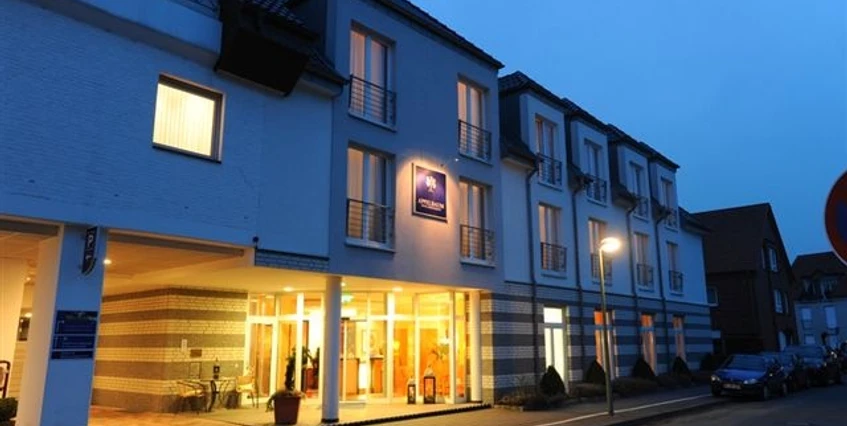 Außenansicht Drei-stöckiges Hotelgebäude bei Abenddämmerung mit beleuchtetem Eingangsbereich und angrenzendem Parkplatz.