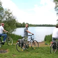 Drei Radfahrer halten mit Blick auf einen ruhigen See und umgeben von grüner Vegetation inne.