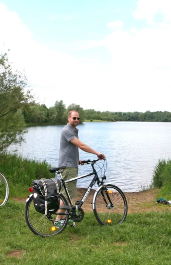 Radfahrer an der "Nienburger Rolle" Drei Radfahrer halten mit Blick auf einen ruhigen See und umgeben von grüner Vegetation inne.
