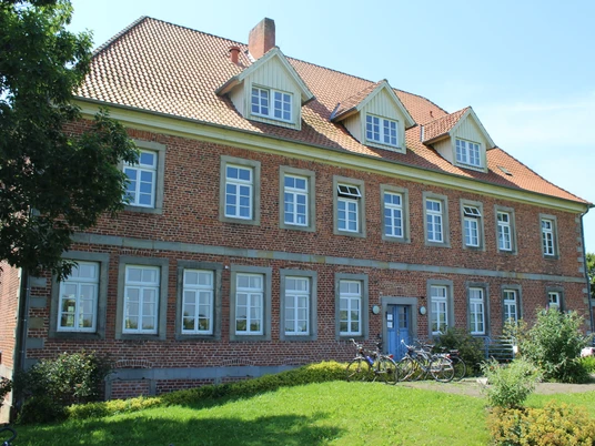Amtshaus Westen mit Heimatstube Backsteinbau mit hohem Dach, symmetrischer Fensterreihe und grüner Umgebung, Fahrräder vor dem Gebäude.