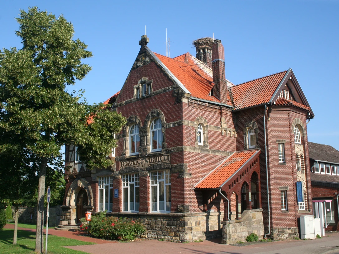 Gemeinde Schule Backsteingebäude der Gemeinde Schule mit roten Dächern, grüner Baum flankiert den Eingangsbereich.