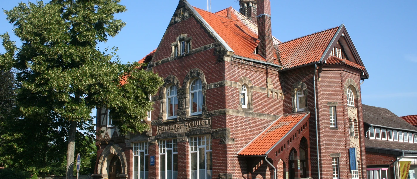 Gemeinde Schule Backsteingebäude der Gemeinde Schule mit roten Dächern, grüner Baum flankiert den Eingangsbereich.