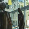 Zwei moderne Bronze-Skulpturen stehen sich gegenüber in einem lichtdurchfluteten Gebäudekomplex.