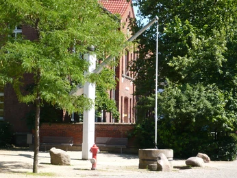 Skulptur Der Hungerbrunnen Rote Backsteinbauten bilden den Hintergrund der metallischen Skulptur "Hungerbrunnen" im Sonnenschein.