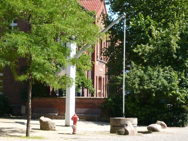 Skulptur Der Hungerbrunnen Rote Backsteinbauten bilden den Hintergrund der metallischen Skulptur "Hungerbrunnen" im Sonnenschein.