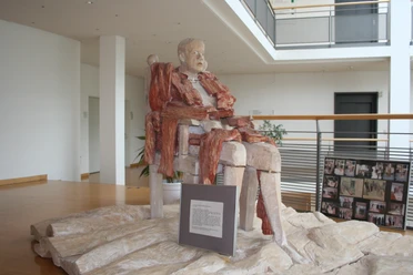 Skulptur Der Patriarch Fijodor Karamasow Eine beeindruckende Skulptur von Fijodor Karamasow, der in einem modernen Innenraum posiert.
