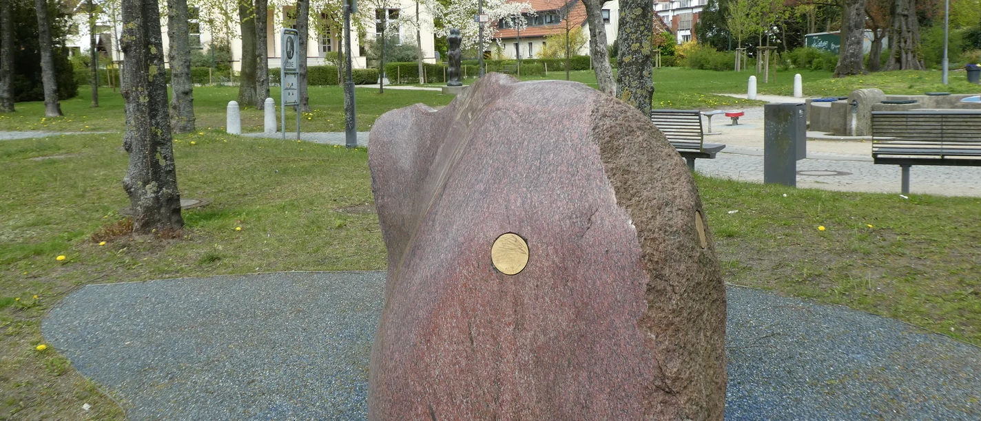 Skulptur "Freund von Weser" Großer, polierter Granitblock mit glatter Oberfläche, im Park auf blauem Kiesbett platziert.