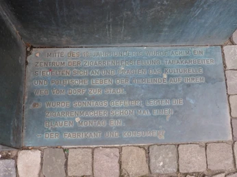 Gedenktafel aus Metall mit Inschrift zur Zigarrenherstellung in Achim, verlegt auf einem Steinboden.