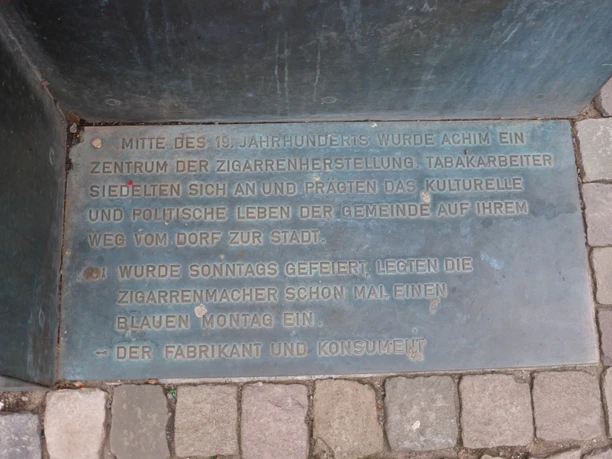 Gedenktafel aus Metall mit Inschrift zur Zigarrenherstellung in Achim, verlegt auf einem Steinboden.