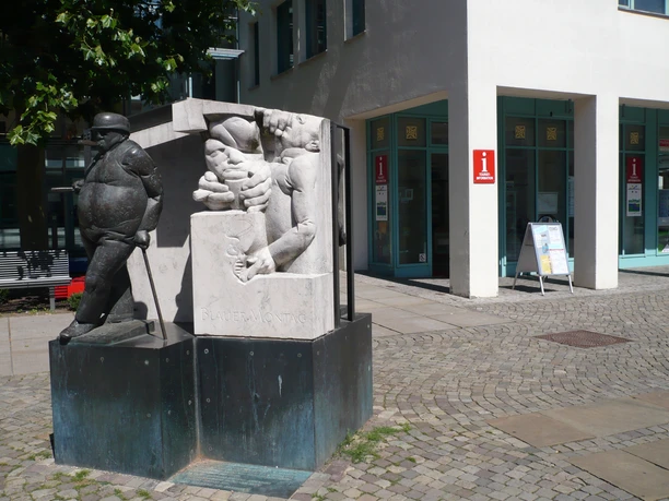 Die Skulptur "Zigarrenmacher" zeigt einen Handwerker, der Zigarren rollt, vor einem modernen Gebäude.