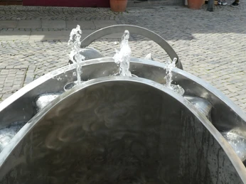 Moderner Brunnen in Achim sprudelt lebendig anmutend aus Edelstahl auf gepflastertem Platz.