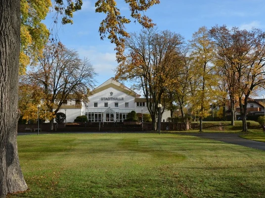 Stadthalle in Brakel Weiße Stadthalle in Brakel umgeben von herbstlichen Bäumen und gepflegtem Rasen, vorne Gehweg.