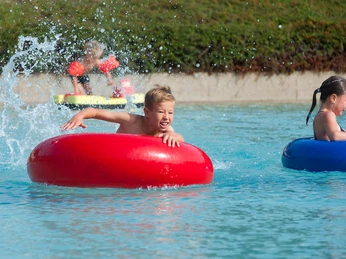 Wasserspaß Hallen- und Freibad Wingst Kinder toben lachend in bunten Schwimmreifen im klaren Wasser des Freibads Wingst.