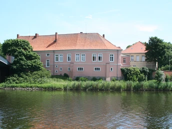 Historisches Schloß Hoya am Ufer eines Flusses, umgeben von Bäumen unter blauem Himmel.