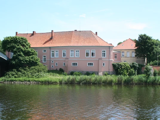 Historisches Schloß Hoya am Ufer eines Flusses, umgeben von Bäumen unter blauem Himmel.Historic Hoya Castle on the banks of a river, surrounded by trees under a blue sky.Det historiske Hoya-slot ligger ved bredden af en flod, omgivet af træer under en blå himmel.Historisch kasteel Hoya aan de oever van een rivier, omringd door bomen onder een blauwe hemel.