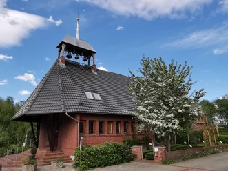 Moorkirche Backsteinkirche mit steilem grauen Dach und offenem Glockenturm, umgeben von blühenden Bäumen.
