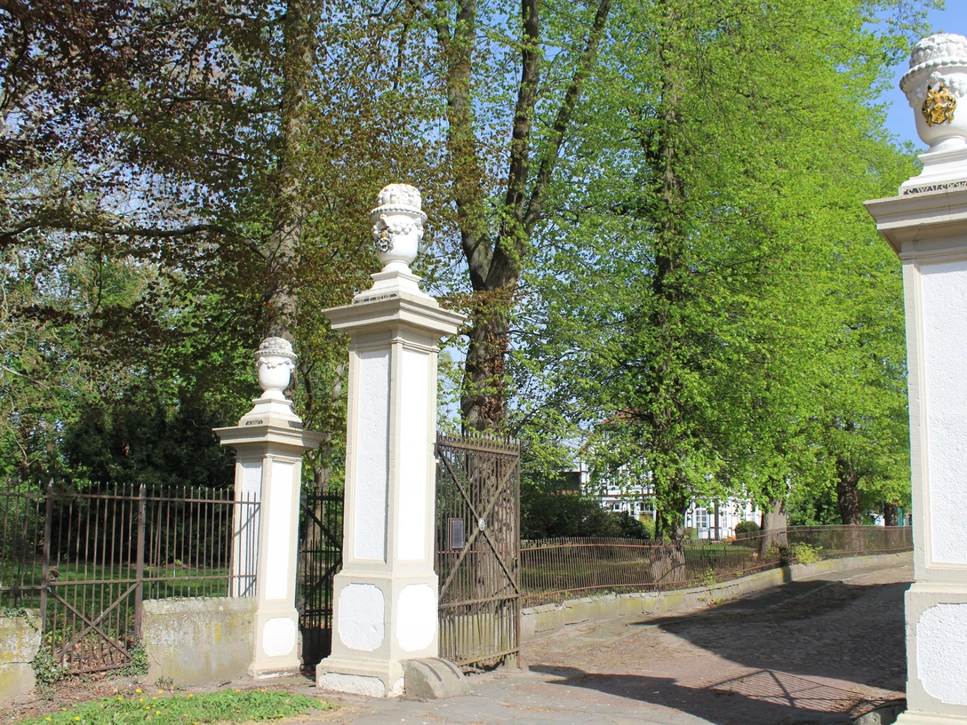 SG Grafschaft Hoya Rittergut von Behr Eingang des historischen Ritterguts von Behr, gesäumt von Säulen mit dekorativen Vasen in ländlicher Umgebung.