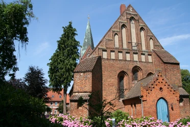 Kirche St. Cosmae und Damiani Backsteinkirche mit spitzem Turm und prächtigen Rosengärten, eingerahmt von blauem Himmel und Bäumen.