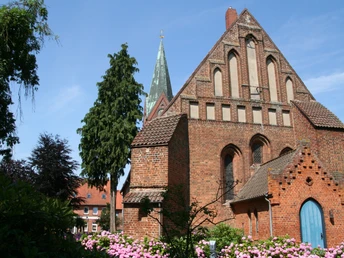 Kirche St. Cosmae und Damiani Backsteinkirche mit spitzem Turm und prächtigen Rosengärten, eingerahmt von blauem Himmel und Bäumen.