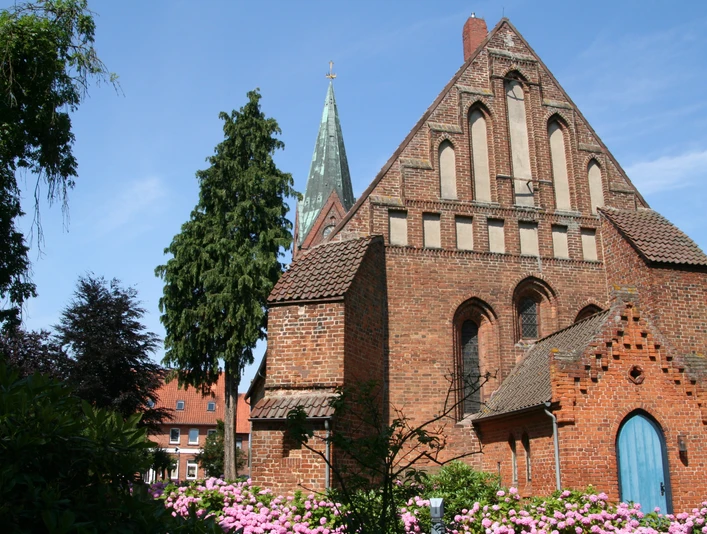 Kirche St. Cosmae und Damiani Backsteinkirche mit spitzem Turm und prächtigen Rosengärten, eingerahmt von blauem Himmel und Bäumen.
