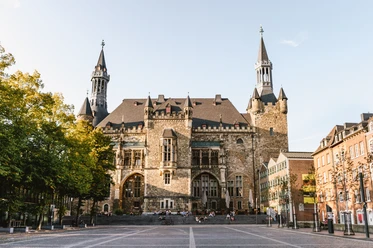 Aachener Rathaus auf Katschhof mit prächtiger Fassade aus Bruchstein, umgeben von alten Bäumen und historischer Architektur.