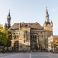 Aachener Rathaus auf Katschhof mit prächtiger Fassade aus Bruchstein, umgeben von alten Bäumen und historischer Architektur.