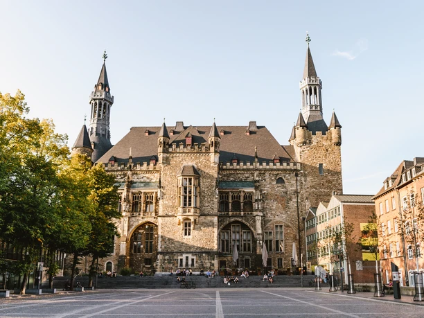 Aachener Rathaus auf Katschhof mit prächtiger Fassade aus Bruchstein, umgeben von alten Bäumen und historischer Architektur.