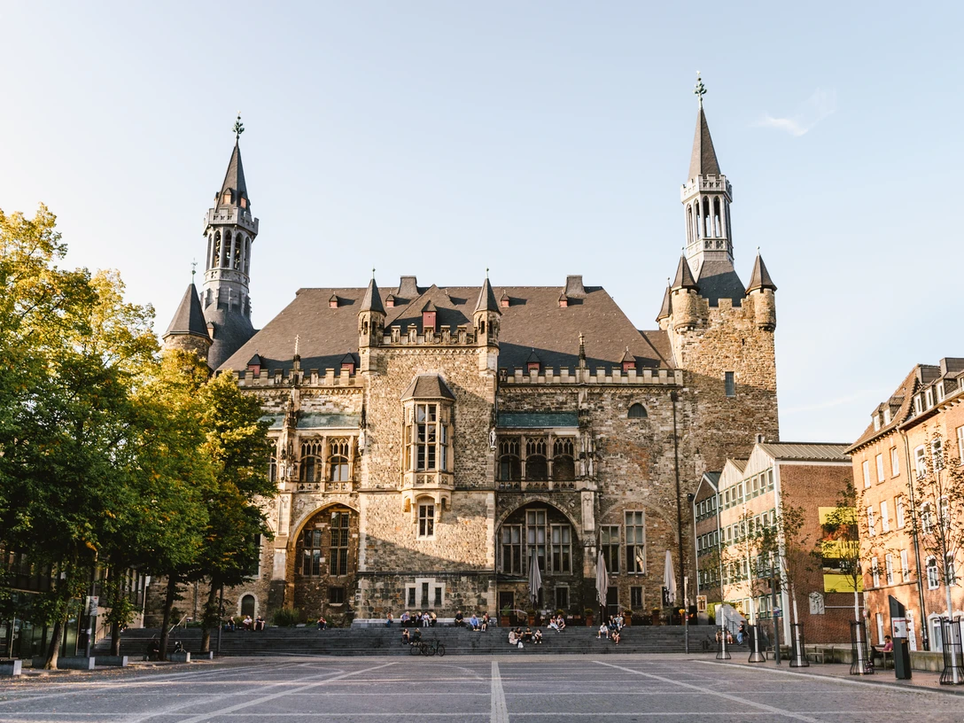 Aachener Rathaus Katschhof.jpg Aachener Rathaus auf Katschhof mit prächtiger Fassade aus Bruchstein, umgeben von alten Bäumen und historischer Architektur.