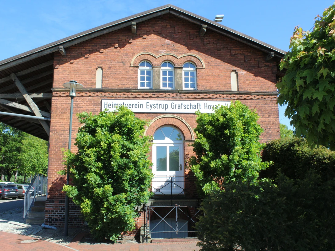 Der historische Backsteingüterschuppen in Eystrup mit grünen Bäumen und einem blauen Himmel.