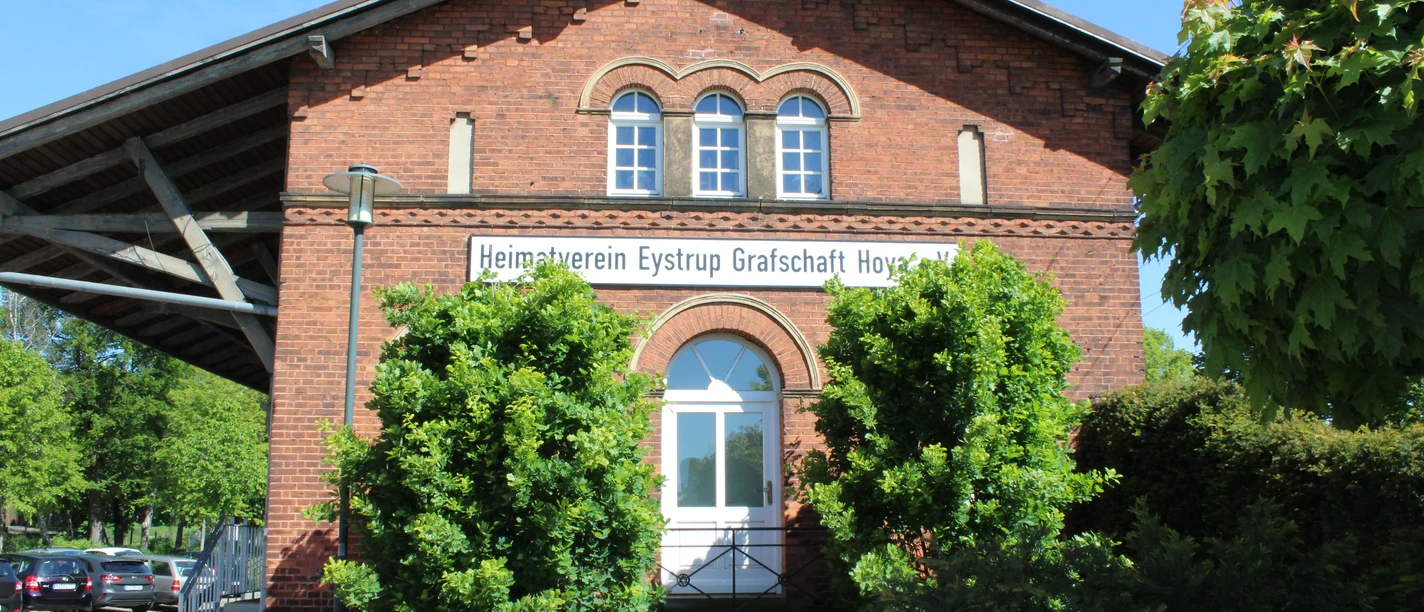 Der historische Backsteingüterschuppen in Eystrup mit grünen Bäumen und einem blauen Himmel.