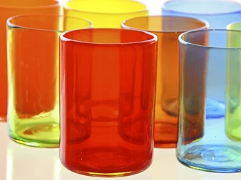 Gernheimer Glas Bunte, leuchtende Gläser in den Farben Orange, Rot, Blau und Gelb auf einer glänzenden Oberfläche.