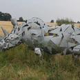 Skulptur Nashorn Eine moderne Nashorn-Skulptur aus Metallplatten steht in einer ländlichen Wiesenlandschaft.