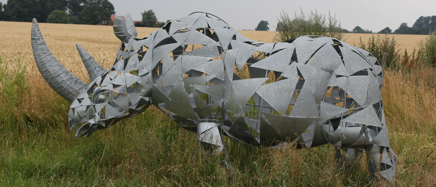 Skulptur Nashorn Eine moderne Nashorn-Skulptur aus Metallplatten steht in einer ländlichen Wiesenlandschaft.
