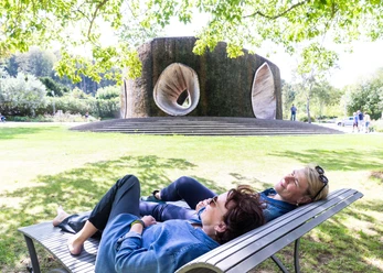 Twee vrouwen relaxen op een bankje voor een grote, sculpturale fontein in het park.