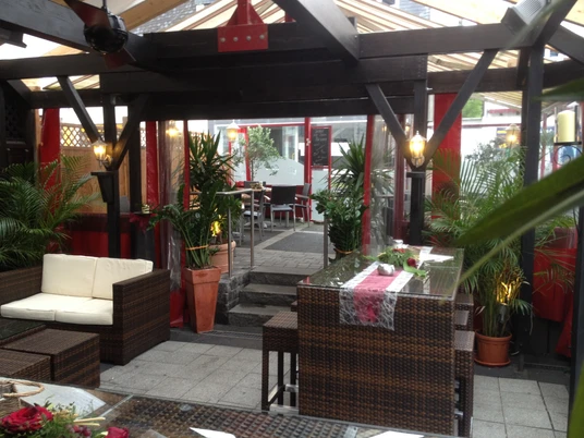 Cafe Pfeil Ein gemütlicher Wintergarten mit Holzbalken, Rattanmöbeln und grünen Pflanzen in einem Restaurant.