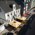Haus Kranenberg Straßenansicht mit mehreren weißen Gebäuden, roten Markisen und gelben Sonnenschirmen vor Cafés.