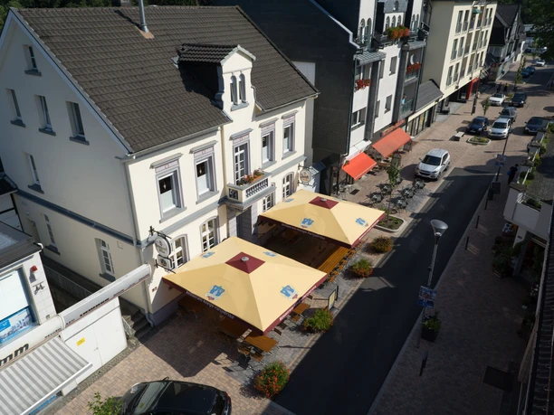 Haus Kranenberg Straßenansicht mit mehreren weißen Gebäuden, roten Markisen und gelben Sonnenschirmen vor Cafés.