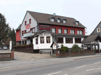 Außenansicht - Landhotel May-Hof Das Bild zeigt ein traditionelles Landhotel mit roter und weißer Fassade, umgeben von Bäumen.
