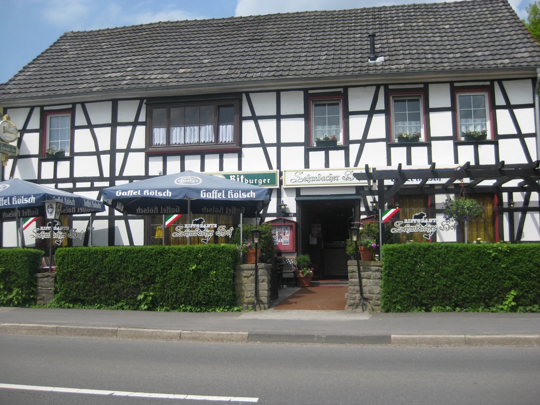 Lehmbacher Hof Fachwerkhaus mit Restaurant. Vor dem Gebäude stehen Biergarten-Sonnenschirme und grüne Hecke.